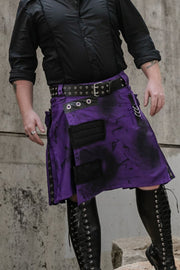Person wearing a purple and black kilt with black leather jacket and boots against a concrete wall.