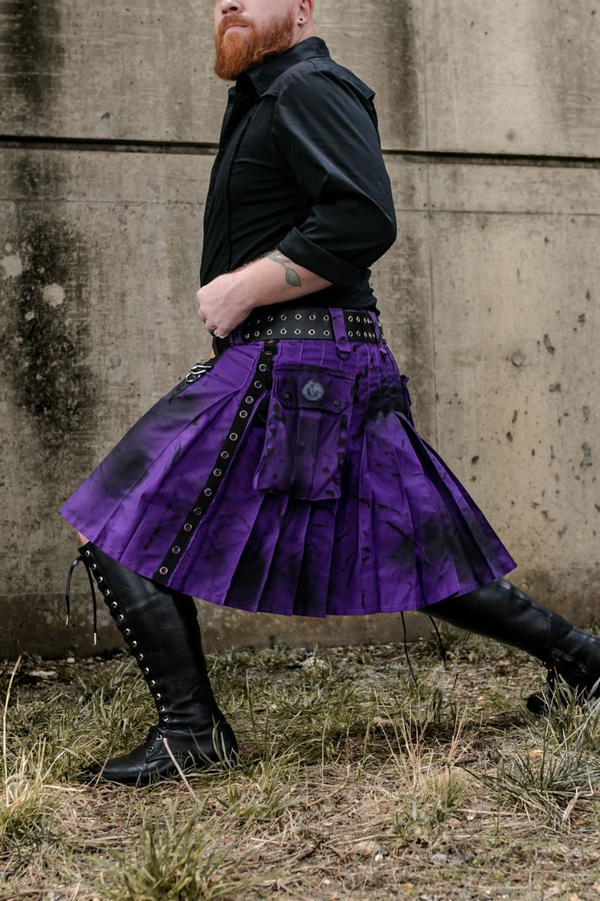 Person wearing a purple kilt with black accents against a concrete wall.
