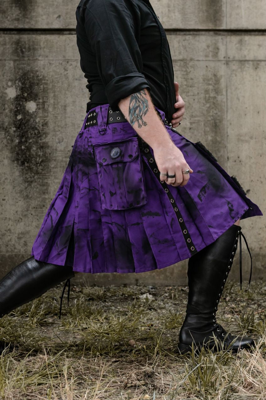 Person wearing a purple kilt with black accents against a concrete wall.